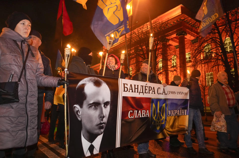 Activists of various nationalist parties carry torches and a portrait of Stepan Bandera during a rally in Kyiv, Ukraine, Saturday, Jan. 1, 2022. The rally was organized to mark the birth anniversary of Stepan Bandera, founder of a rebel army that fought against the Soviet regime and who was assassinated in Germany in 1959. (AP Photo/Efrem Lukatsky)