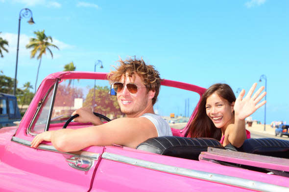 Couple happy in vintage retro convertible car. Friends driving on summer road trip in pink car. Beautiful young Caucasian man an