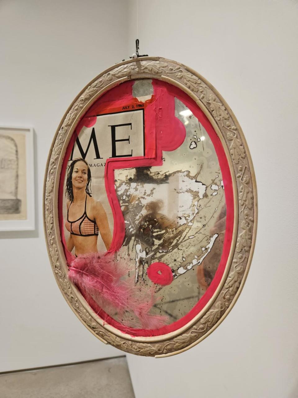 A fragment of a Time magazine cover with the "TI" clipped off, showing a woman in a bikini, pasted on an oval mirror.