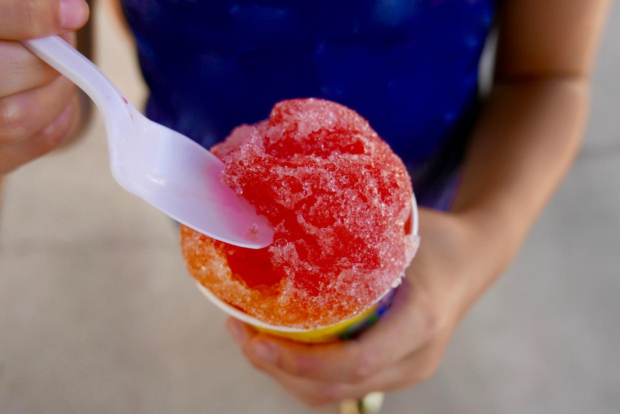 Close up of a colorful snow cone being eaten by a child with a plastic spoon