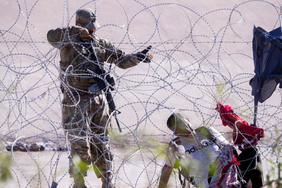 A Texas National Guard soldier lifts a section of concertina wire to allow a migrant to exit south back to the Rio Grande on Sept. 19, 2023. The migrant had spent two days without food or water as he waited to be processed by Border Patrol. The migrant had crossed the Rio Grande from Mexico to El Paso, Texas, in hopes of seeking asylum in the U.S.