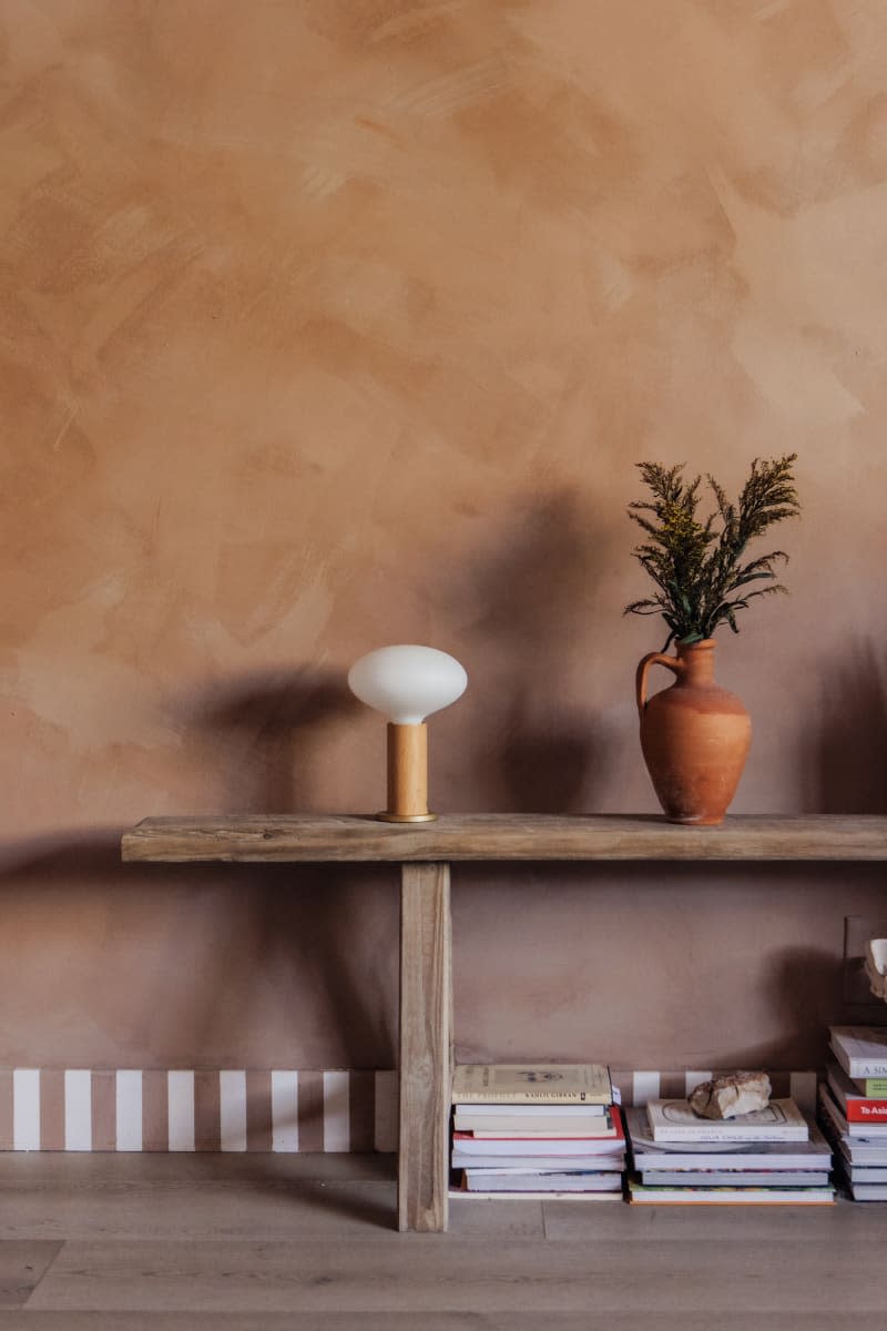 Wood bench in front of textured warm colored wall with books