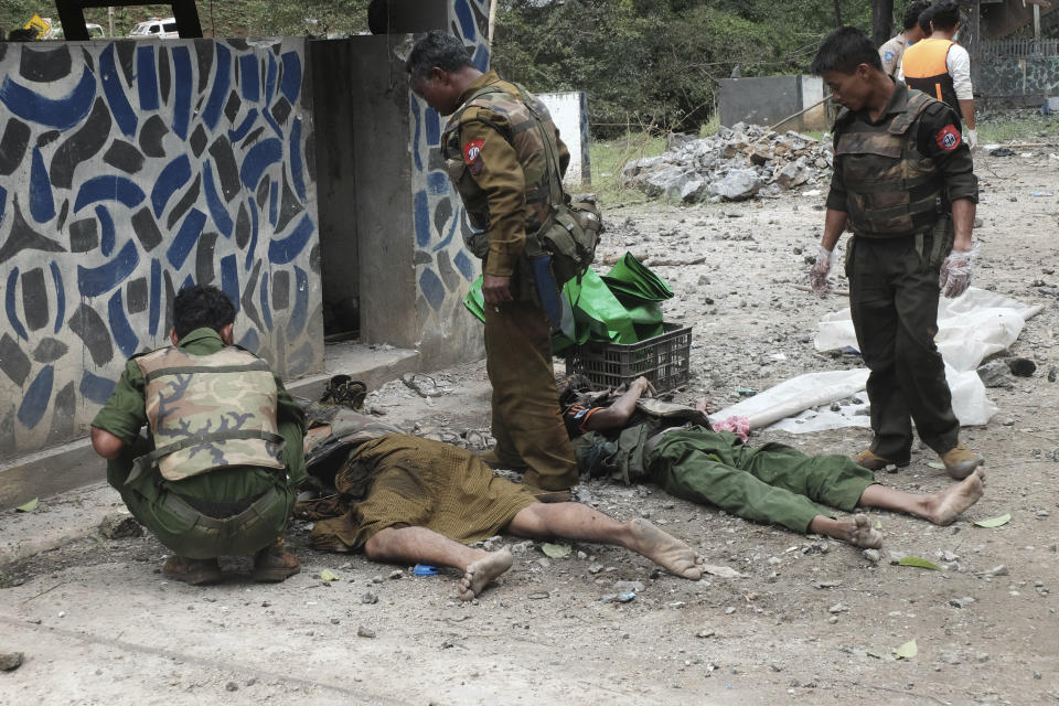 Soldiers stand near two dead bodies at Gote Twin police outpost after an attack Thursday, Aug. 15, 2019, in Gote Twin, Naung Cho township, northern Shan State, Myanmar. Members of an ethnic rebel alliance in Myanmar staged coordinated attacks in five locations Thursday in Mandalay Region and in northern Shan State, where 14 people were reported killed. The group said the attacks were a response to government military operations in territory where the Kokang, Ta-ang and Rakhine minorites live. (AP Photo/Pyae Sone Aung)