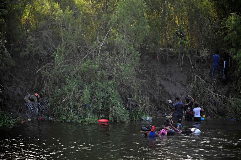 Migrantes cruzan el río Bravo mientras miembros de la Guardia Nacional de EE. UU. colocan una barrera de alambre de púas a lo largo del río en la frontera entre EE. UU. y México, visto desde Matamoros, estado de Tamaulupas, México, el 10 de mayo de 2023