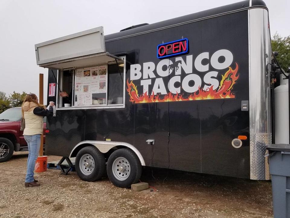 A customer picks up an order at Bronco Tacos before sitting down to eat at one of two picnic tables on the lot.