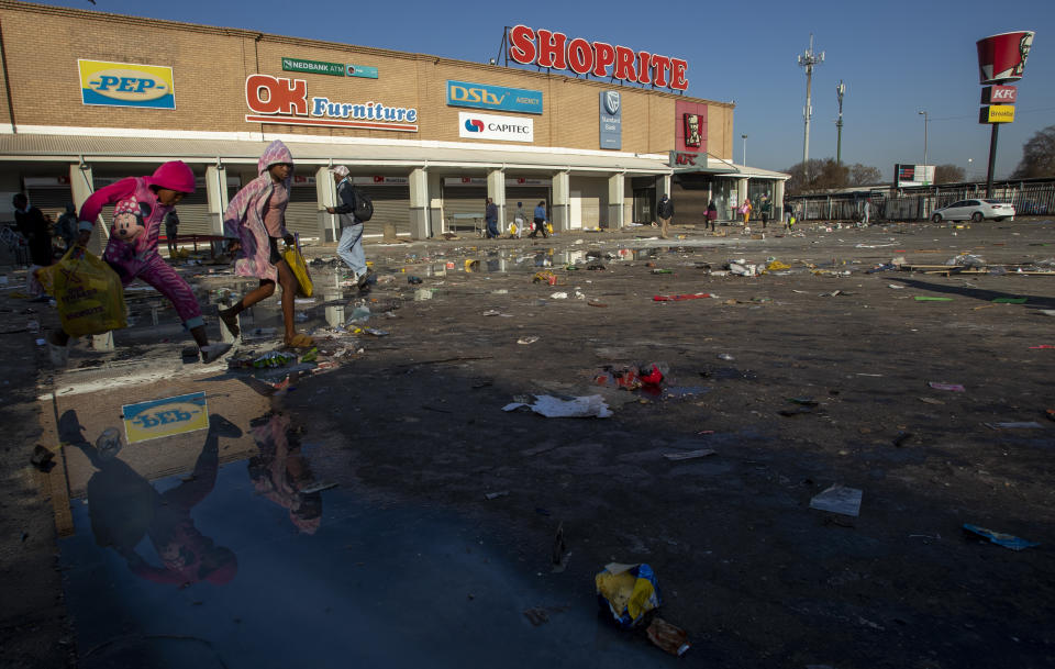 Young girls carrying groceries looted from a nearby shop, jump over the puddle of water back home at Naledi shopping complex in Vosloorus, east of Johannesburg, South Africa, Monday, July 12, 2021. Police say six people are dead and more than 200 have been arrested amid escalating violence during rioting that broke out following the imprisonment of South Africa's former President Jacob Zuma. (AP Photo/Themba Hadebe)