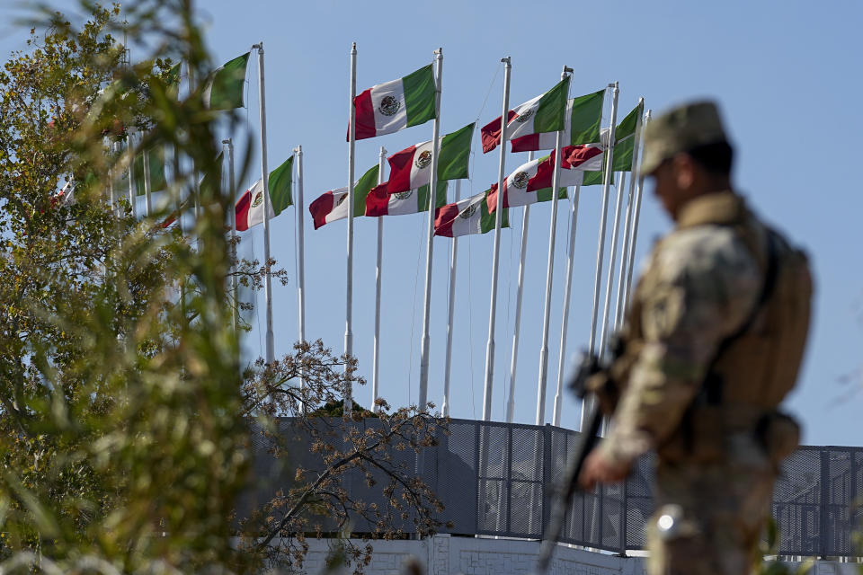 A guardsman keeps watch along the Rio Grande with flags seen on the Mexico side, Wednesday, Jan. 3, 2024, in Eagle Pass, Texas. U.S. House Speaker Mike Johnson is leading about 60 fellow Republicans in Congress on a visit to the Mexican border. Their trip comes as they are demanding hard-line immigration policies in exchange for backing President Joe Biden's emergency wartime funding request for Ukraine. Senate negotiators in Washington are plugging away in hopes of a bipartisan deal. The number of illegal crossings into the United States topped on several days last month. (AP Photo/Eric Gay)