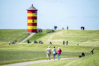 Tourists walk on the dike in front of the Pilsum lighthouse in the municipality of Krummhoern, Germany, Thursday, may 28, 2020. The lighthouse with its red-yellow striped painting served as a backdrop for several feature films. Since 2004 it is also used for civil weddings. (Hauke-Christian Dittrich/dpa via AP)