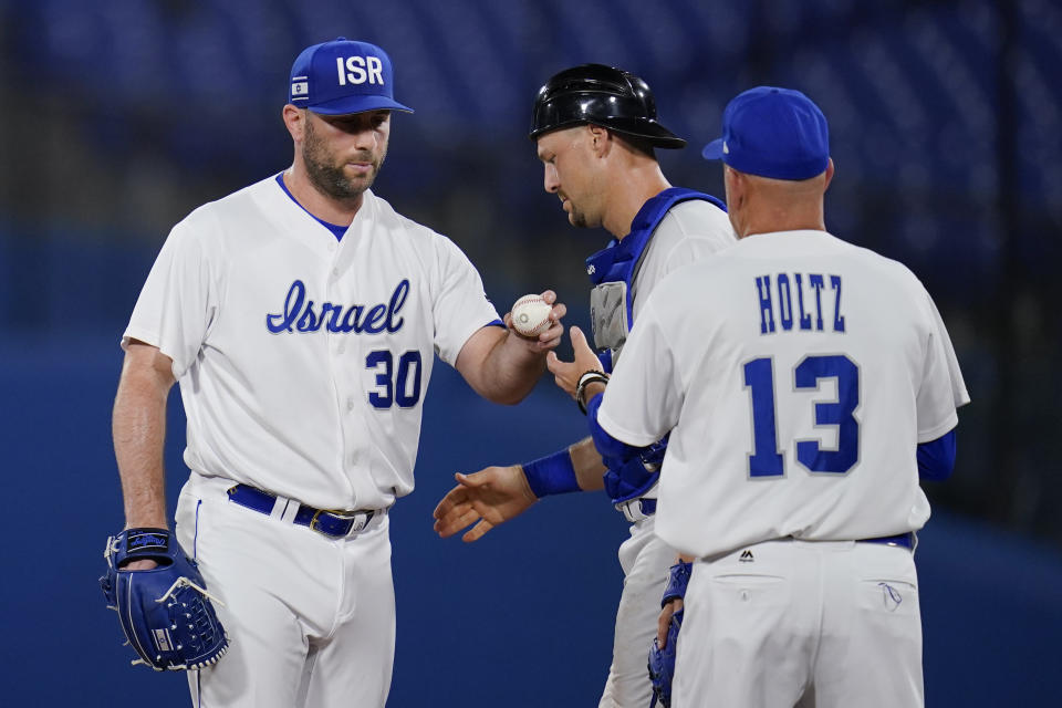 Israel's Jeremy Bleich, left hands the ball to manager Eric Holtz, right, as Ryan Lavarnway looks on during the sixth inning of a baseball game against the United States at the 2020 Summer Olympics, Friday, July 30, 2021, in Yokohama, Japan. (AP Photo/Sue Ogrocki)