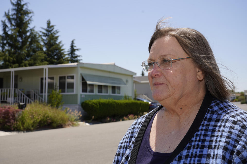 In this June 29, 2021, photo, Judy Pavlick, 74, poses outside where she lives at a mobile home park in Sunnyvale, Calif. Newly retired, Pavlick was among hundreds of seniors who enjoyed the low cost-of-living and friendly atmosphere at Plaza Del Rey, a sprawling mobile home park in Sunnyvale. Then the Carlyle Group acquired the property and things began to change. Pavlick's rent surged by more than 7%. Additional increases followed. She said the unexpected jump forced her and her neighbors, many on fixed incomes and unable to relocate, to sometimes choose between food and medicine. (AP Photo/Eric Risberg)