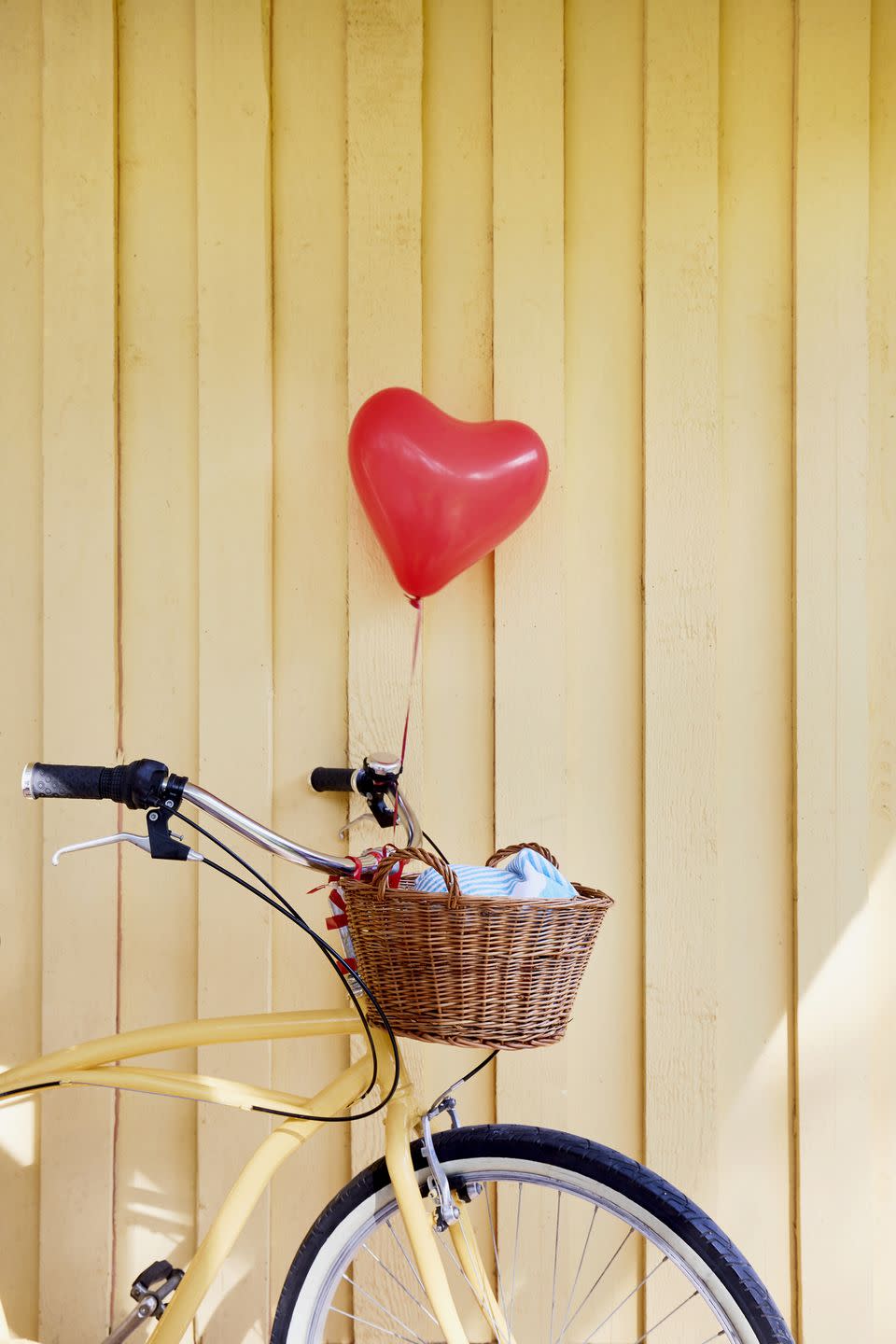 yellow beachcruiser bicycle with a red balloon in heart shape at yellow wooden wall