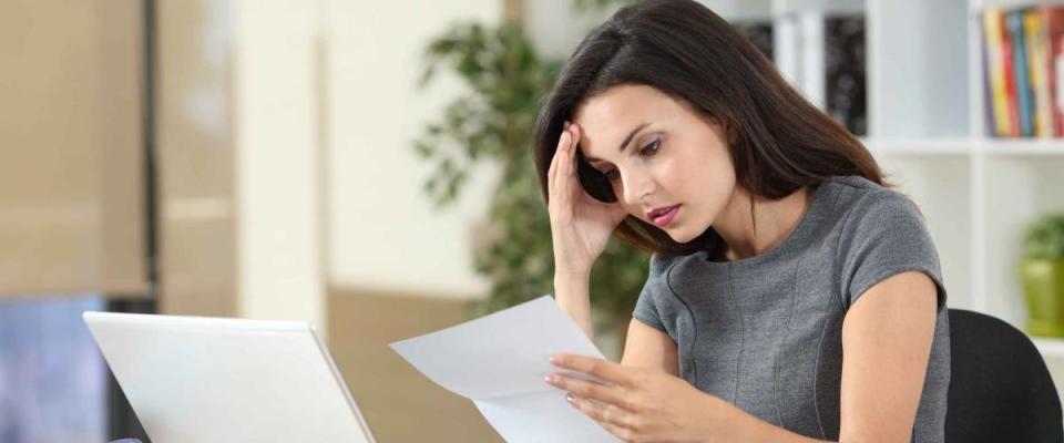 Woman looks down at a piece of paper and holds her head in her hand.