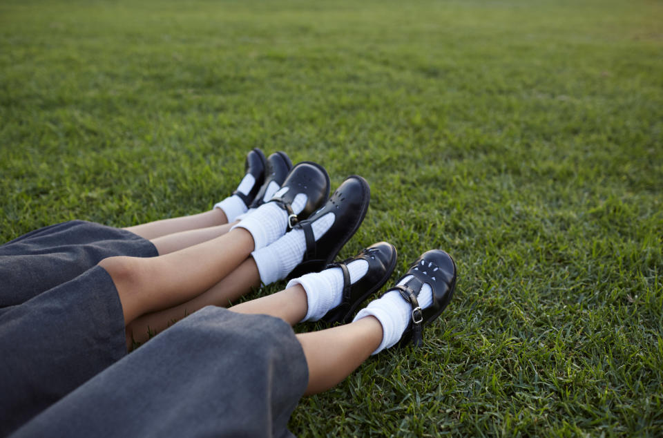 Three pairs of children's legs in school uniforms lying on the lawn