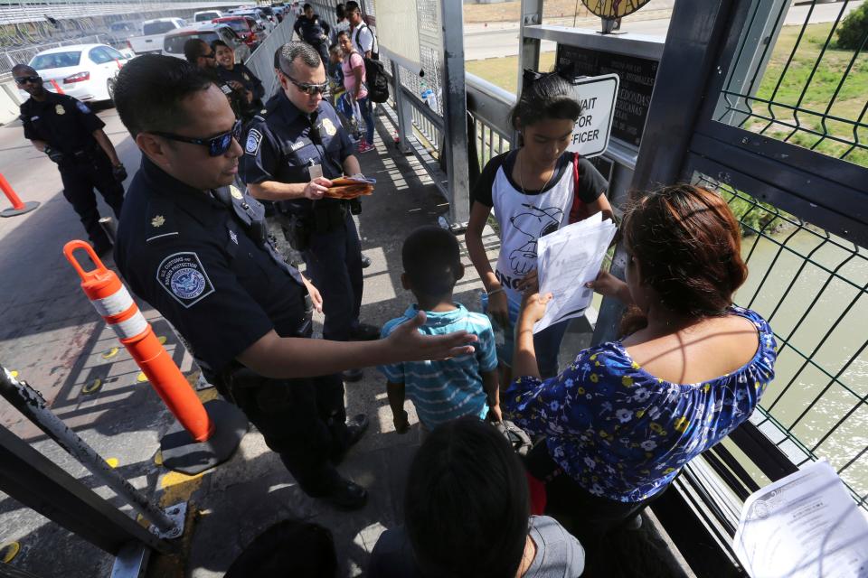 In this July 17, 2019, file photo, a United States Customs and Border Protection Officer checks the documents of migrants before being taken to apply for asylum in the United States, on International Bridge 1 in Nuevo Laredo, Mexico. On Wednesday, July 24, 2019, a federal judge in San Francisco blocked the Trump administration's asylum restrictions at the U.S.-Mexico border.