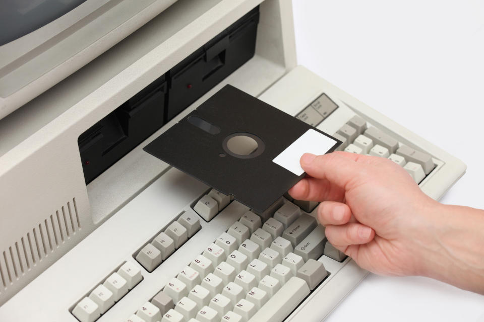 Hand inserting old floppy disk into a vintage old computer from the eighties, with integrated disk drive monitor and keyboard. Retro revival style with rounded corners.