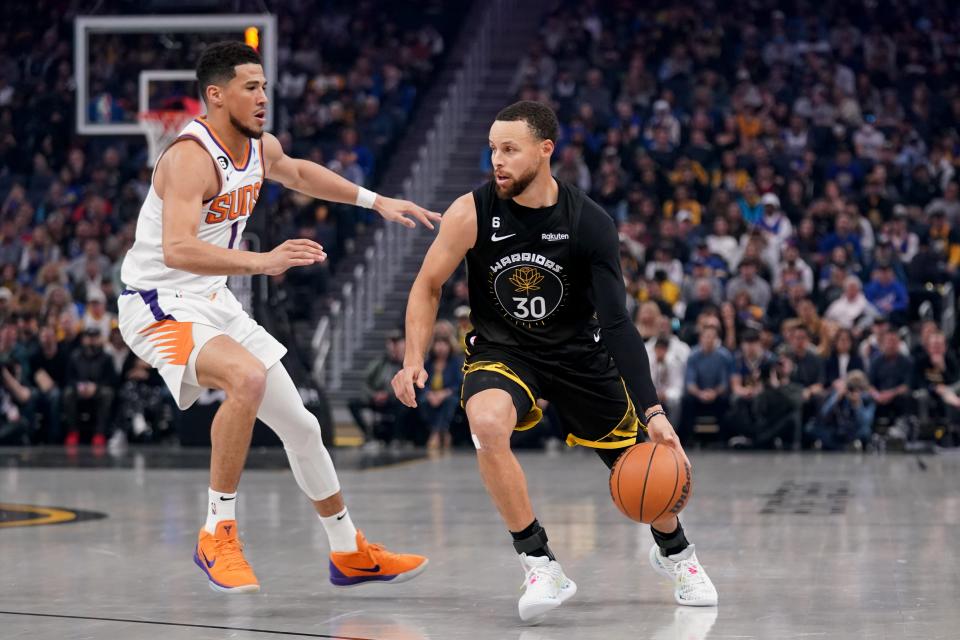 Le garde des Golden State Warriors Stephen Curry (30 ans) dribble devant le garde des Phoenix Suns Devin Booker (1) au premier trimestre au Chase Center de San Francisco le 13 mars 2023.