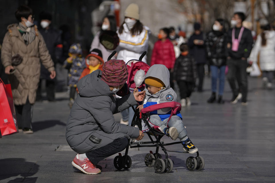 A woman feeds snack food to a child on a stroller at Qianmen pedestrian shopping street, a popular tourist spot in Beijing, Tuesday, Jan. 17, 2023. China has announced its first population decline in decades as what has been the world's most populous nation ages and its birthrate plunges. (AP Photo/Andy Wong)