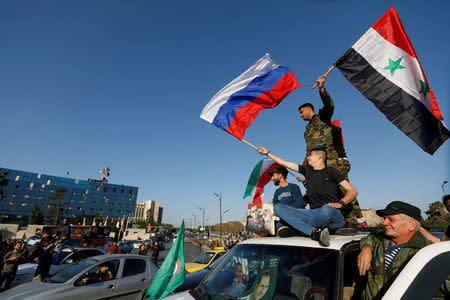 Syrians wave Russian and Syrian flags during a protest against U.S.-led air strikes in Damascus,Syria April 14,2018.REUTERS/ Omar Sanadiki