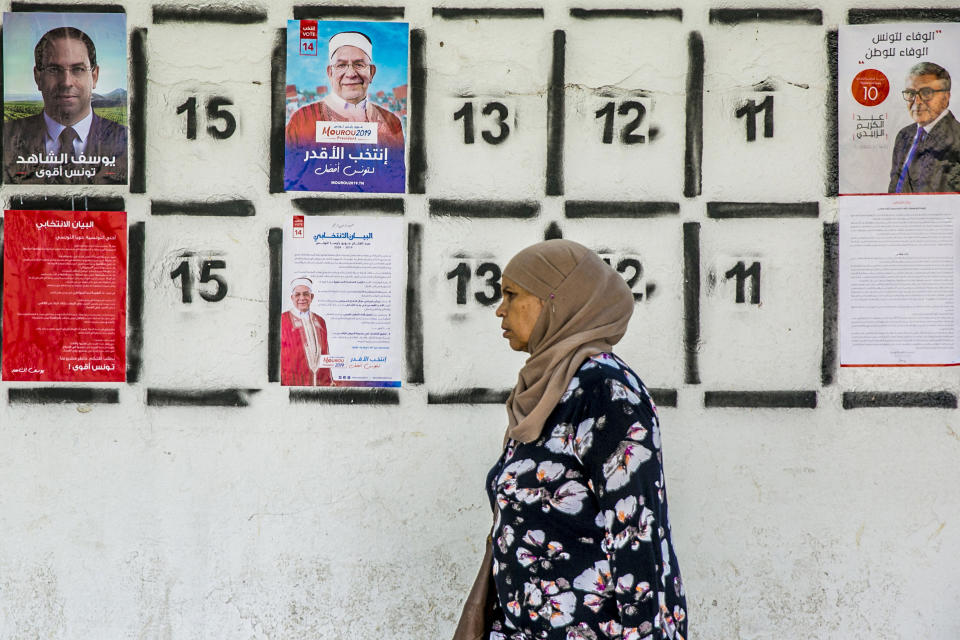 A woman walks past a wall of campaign posters in Tunis, Tunisia, Monday, Sept. 2, 2019.Tunisia's 26 presidential candidates have launched their campaigns in a political climate marked by uncertainty, money laundering allegations and worries about violent extremism. (AP Photo/Hassene Dridi)