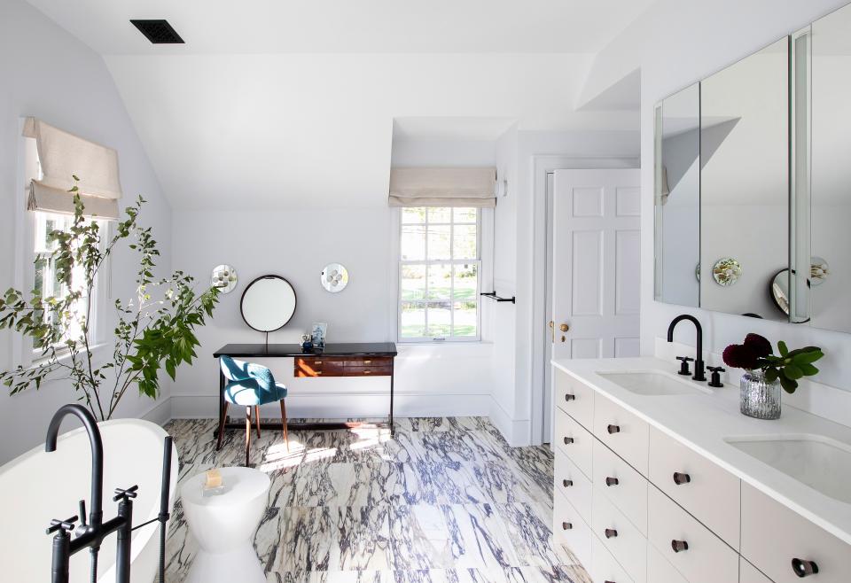 In the primary bathroom, a tub by Apaiser and stone floors by Virtue Tile give the space a timeless look. Galli says she made “the room a little more magical” with a vintage wooden makeup vanity. The sconces above the makeup vanity are from Souda. The vanity is by Orchard Design, and the window coverings are by Fawn Galli Interiors.