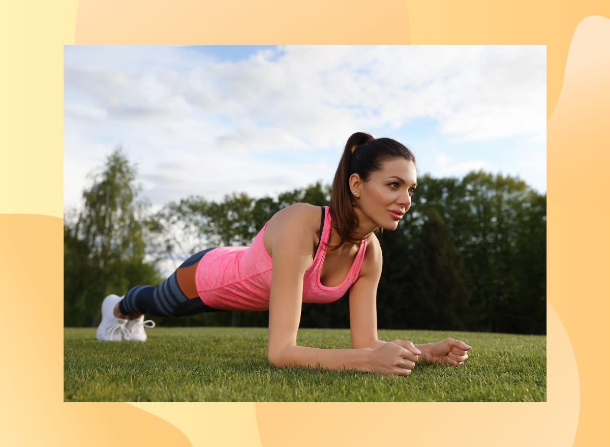 fit brunette woman wearing pink tank, leggings, and white sneakers doing forearm plank exercise in park