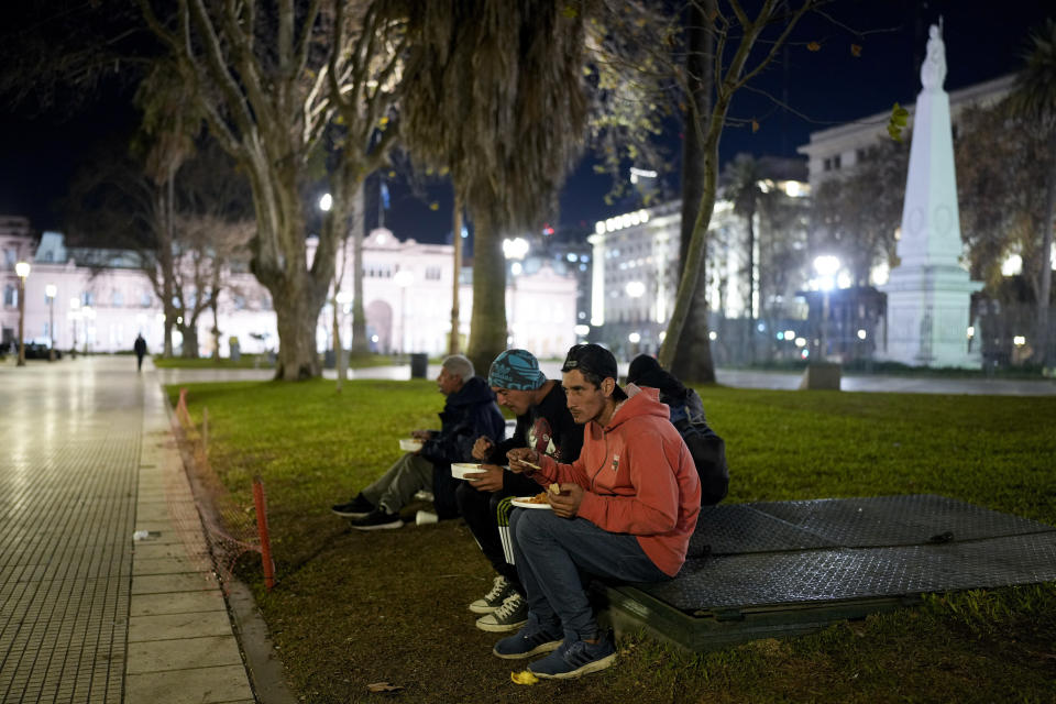 Armando Fernández (delante) y Mariano Quinteros toman la comida que reparte el grupo "Red Solidaria" en un comedor benéfico al aire libre que se instala cada noche en la Plaza de Mayo, a unos metros de la sede del gobierno, la Casa Rosada, en Buenos Aires, Argentina, el 1 de julio de 2024. El mes pasado, Fernández recorrió a pie cientos de kilómetros desde su empobrecida ciudad natal, Santa Fe, en el sur, para buscar trabajo. Ahora barre las sucias aceras de la capital a cambio de los pesos que los dueños de los negocios quieran darle. (AP Foto/Natacha Pisarenko)