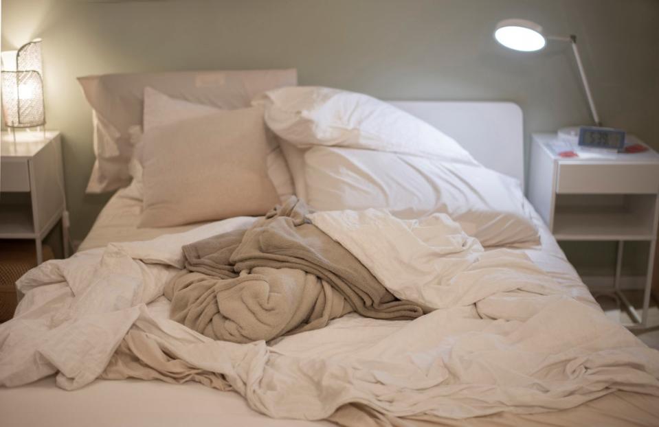 Unmade bed with beige and white sheets, with lamps on nightstands around bed