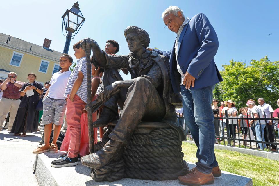 Richard Blake places his arm around the statue of Frederick Douglass he made, during the Abolition Row Park dedication in New Bedford.