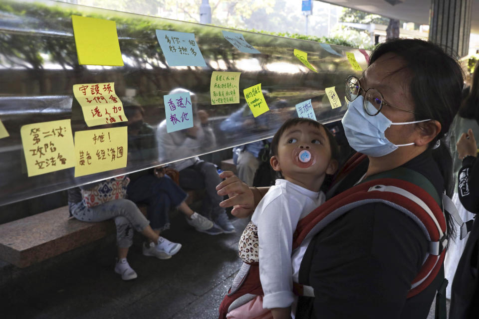 A woman holds a child as she looks at notes on a Lennon wall during a rally for students and elderly pro-democracy demonstrators in Hong Kong, Saturday, Nov. 30, 2019. Hundreds of Hong Kong pro-democracy activists rallied Friday outside the British Consulate, urging the city's former colonial ruler to emulate the U.S. and take concrete actions to support their cause, as police ended a blockade of a university campus after 12 days. (AP Photo/Ng Han Guan)