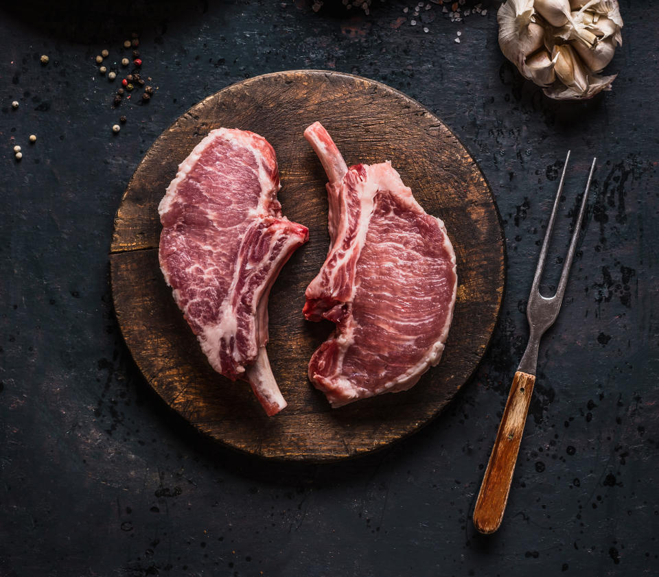 Marbled raw pork chops of Porco Iberico meat on round cutting board with meat knife on dark rustic background, top view. French Racks