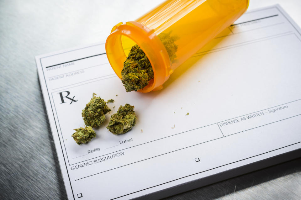 A tipped over prescription bottle containing dried cannabis flower that's lying atop a doctor's prescription pad.