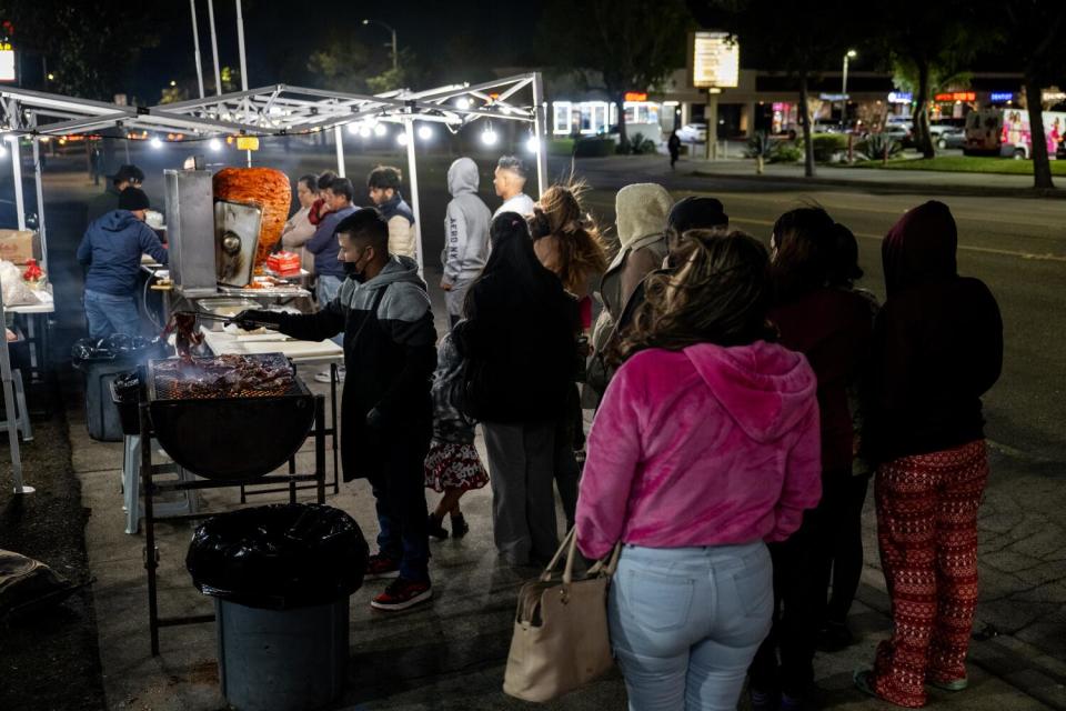 A crowd forms at a taco stand at night.