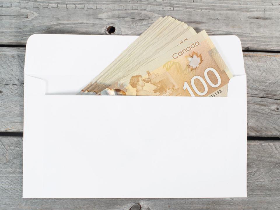 Canadian 100 bills in white envelope on a wooden table