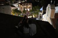 Youths sit atop of a building as people enjoy during a festivity, known as Panigiri, on the Aegean Sea island of Tzia or Kea, Greece, early Tuesday, Aug. 16, 2022. The Dormition of the Virgin Mary (or Mother of God as the Greeks usually refer to her) is celebrated on Aug. 15. The religious event is coupled with midsummer festivities, known as Panigiria, that often last more than a day with music, culinary feasts and, in many cases, flea markets. (AP Photo/Thanassis Stavrakis)