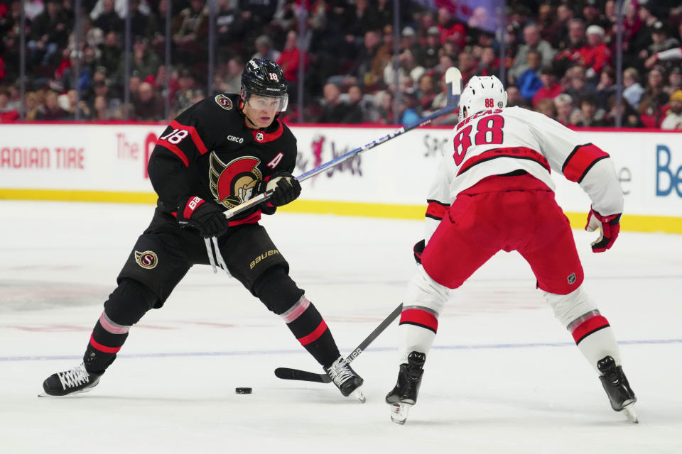Ottawa Senators center Tim Stutzle (18) passes the puck between his legs as he moves around Carolina Hurricanes center Martin Necas (88) during the second period of an NHL hockey match in Ottawa, Ontario, on Tuesday, Dec. 12, 2023. (Sean Kilpatrick/The Canadian Press via AP)