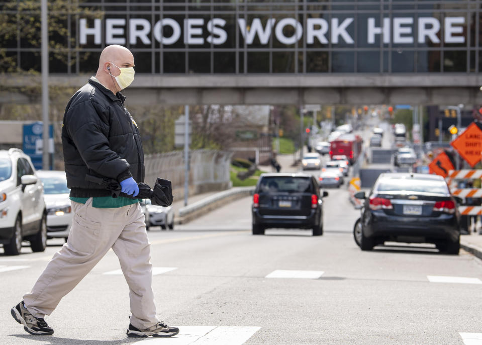 A UPMC Shadyside employee, who declined to give his name, walks to a bus stop near UPMC Shadyside's overpass decorated with signage reading "Heroes work here," during the COVID-19 pandemic Tuesday, April 21, 2020, in Pittsburgh. UPMC officials said Tuesday that patients coming into its hospitals would be tested for COVID-19 along with the system's medical staff, with the eventual goal of working with public health officials in broad public testing. (Steph Chambers/Pittsburgh Post-Gazette via AP)