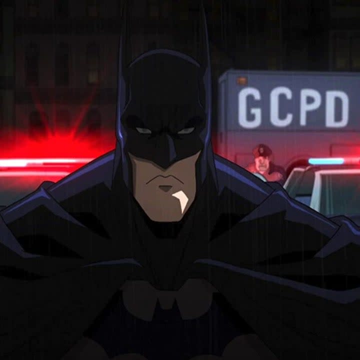 Batman with his back turned to an officer pointing his gun to his bac from his squad car