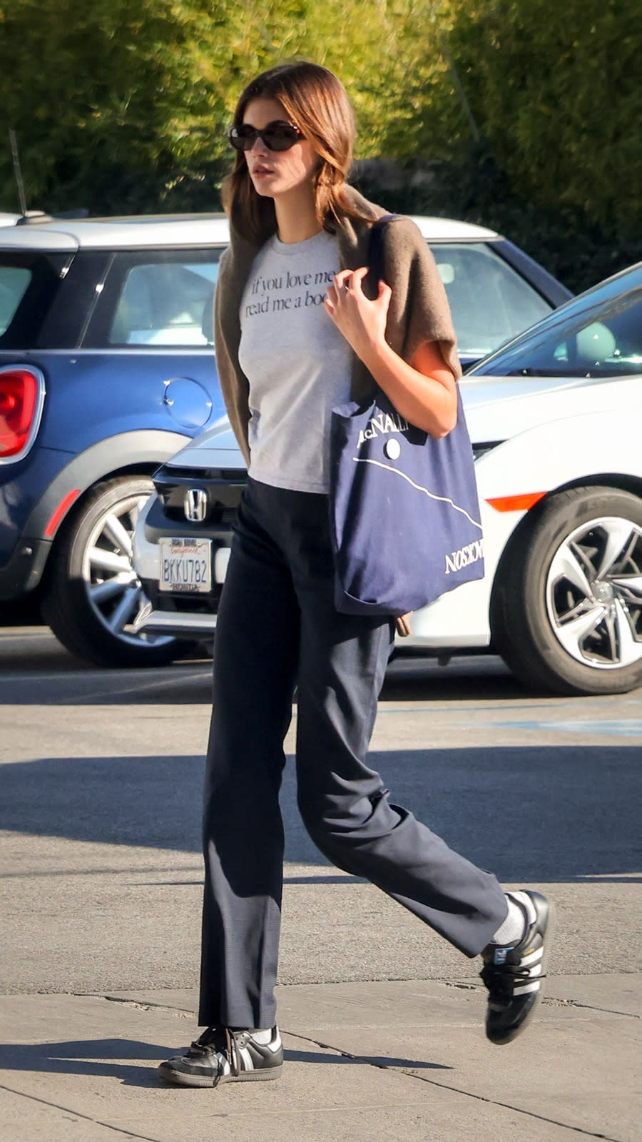 Kaia Gerber wearing a grey tee-shirt with a blue tote bag and Adidas Sambas