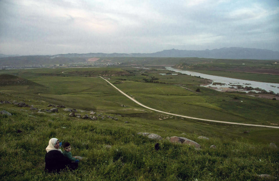 FILE - In this file photo dated Wednesday, May 1, 2019, a woman and child sit on a hill overlooking the Euphrates River as families picnic on May Day, in Derik, Syria. Turkey wants to establish a safe zone up to 25 miles (40 kilometers) deep, east of the Euphrates River in Syria, that effectively amounts to almost all the territory in northeastern Syria that is currently controlled by Syrian Kurdish fighters from the People’s Protection Units, or YPG. (AP Photo/Baderkhan Ahmad, FILE)