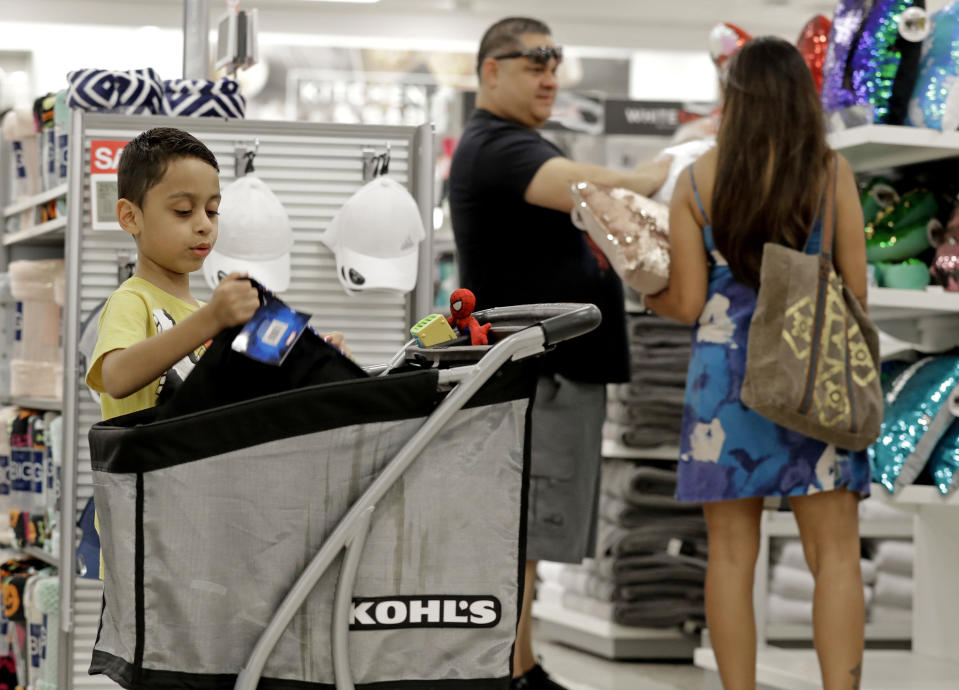 In this Tuesday, Aug. 28, 2018, photo Mark Vega, 7, left, looks inside his family’s cart as parents Frankie Vega, center, and Kimberly Vega, right, shop at a Kohl’s store in Concord, N.C. Many kinds of chains have posted strong sales, both online and at stores. A booming economy, which has shoppers spending more freely, and companies’ own efforts in trying to Amazon-proof their business is driving people’s mood to spend. (AP Photo/Chuck Burton)