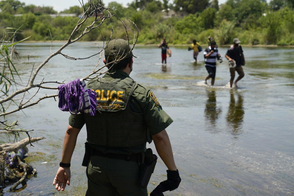FILE - A Border Patrol agent watches as a group of migrants walk across the Rio Grande on their way to turn themselves in upon crossing the U.S.-Mexico border in Del Rio, Texas, on June 15, 2021. The Supreme Court has certified its month-old ruling allowing the Biden administration to end a cornerstone Trump-era border policy to make asylum-seekers wait in Mexico for hearings in U.S. immigration court. It was a pro forma act that has drawn attention amid near-total silence from the White House about when, how and even whether it will dismantle the policy. (AP Photo/Eric Gay, File)