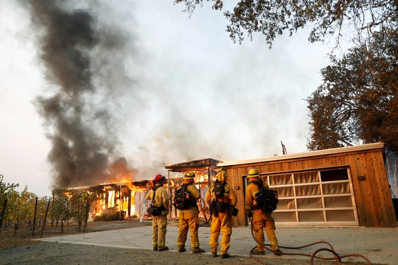 A group of firefighters look on as a house burns during the wind-driven Kincade Fire in Healdsburg, California