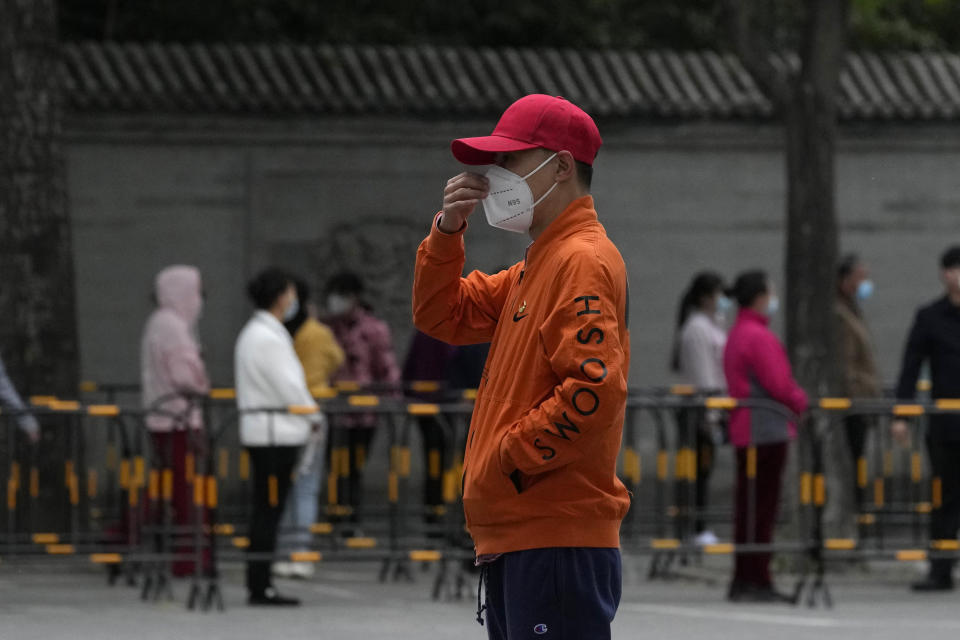 A volunteer wearing a red cap adjusts his mask as residents line up for mass COVID test, Wednesday, April 27, 2022, in Beijing. Workers put up fencing and police restricted who could leave a locked-down area in Beijing on Tuesday as authorities in the Chinese capital stepped up efforts to prevent a major COVID-19 outbreak like the one that has all but shut down the city of Shanghai. (AP Photo/Ng Han Guan)