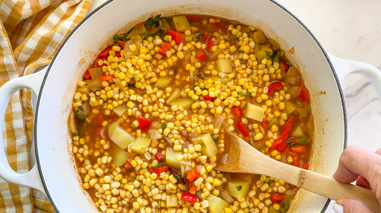 Hand mixing corn into pot of ingredients