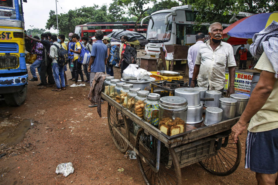 A tea seller with a face mask hanging on his chin talks to a customer beside his movable cart as commuters jostle for a ride on a bus discarding social distancing guidelines in Kolkata, India, Tuesday, July 21, 2020. With a surge in coronavirus cases in the past few weeks, state governments in India have been ordering focused lockdowns in high-risk areas to slow down the spread of infections. (AP Photo/Bikas Das)