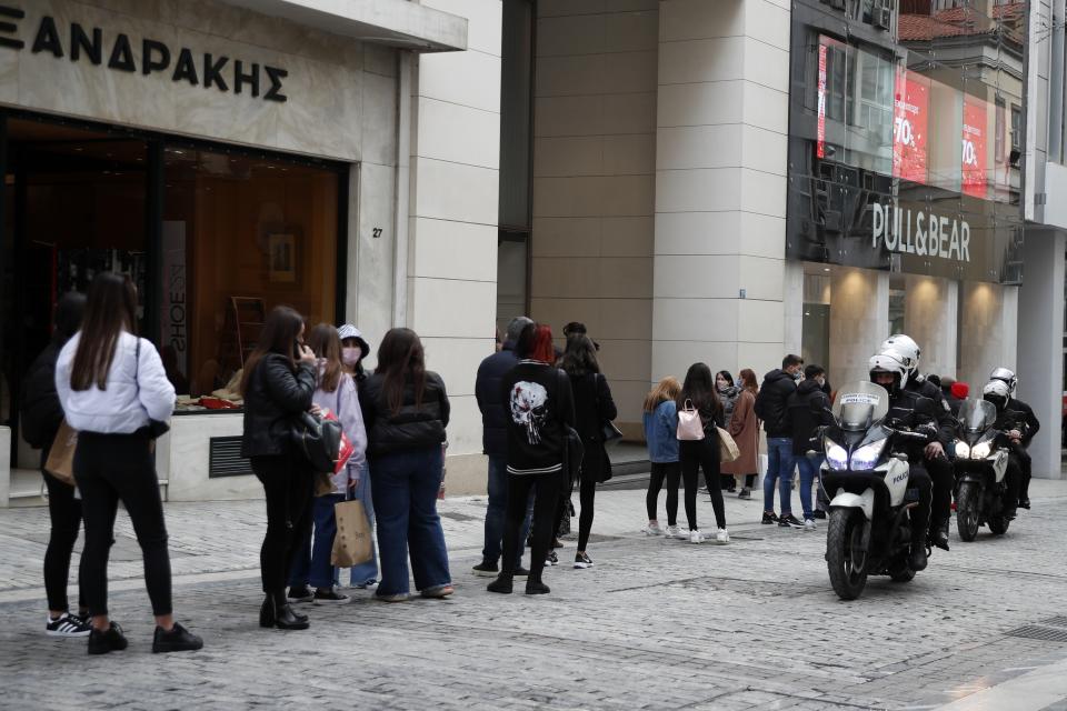 Youths stand in a queue outside a clothes shop as police patrol on Ermou Street, Athens' main shopping area, Friday, Jan. 22, 2021. Greece's government has extended nationwide lockdown measures indefinitely but retail stores and malls reopened Monday with strict entrance limits. (AP Photo/Thanassis Stavrakis)