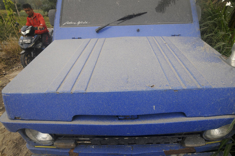 A motorist rides past by as a car is seen covered in volcanic ash from the eruption of Mount Marapi in Agam, West Sumatra, Indonesia, Tuesday, Dec. 5, 2023. Rescuers searching the hazardous slopes of Indonesia's Marapi volcano found more bodies among the climbers caught by a surprise eruption two days ago. (AP Photo/Ardhy Fernando)