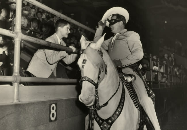 Actor Brace Beemer, dressed as The Lone Ranger, greets a fan inside a stadium.