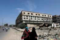 Women walk along a road with an abandoned building of a garment factory in the background, where over 260 people were killed after a fire broke in 2012, in Karachi