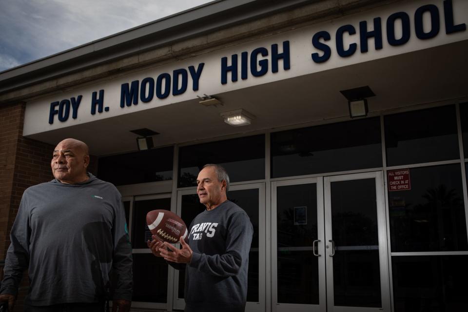 Former Moody halfback Raymond Huff, 68, of Corpus Christi, left, and former quarterback Abbey Cardenas, 67, of Dallas, stand in front of the high school's entrance on Wednesday, Nov. 22, 2023, in Corpus Christi, Texas. Cardenas tosses a ball back and forth in his hands.